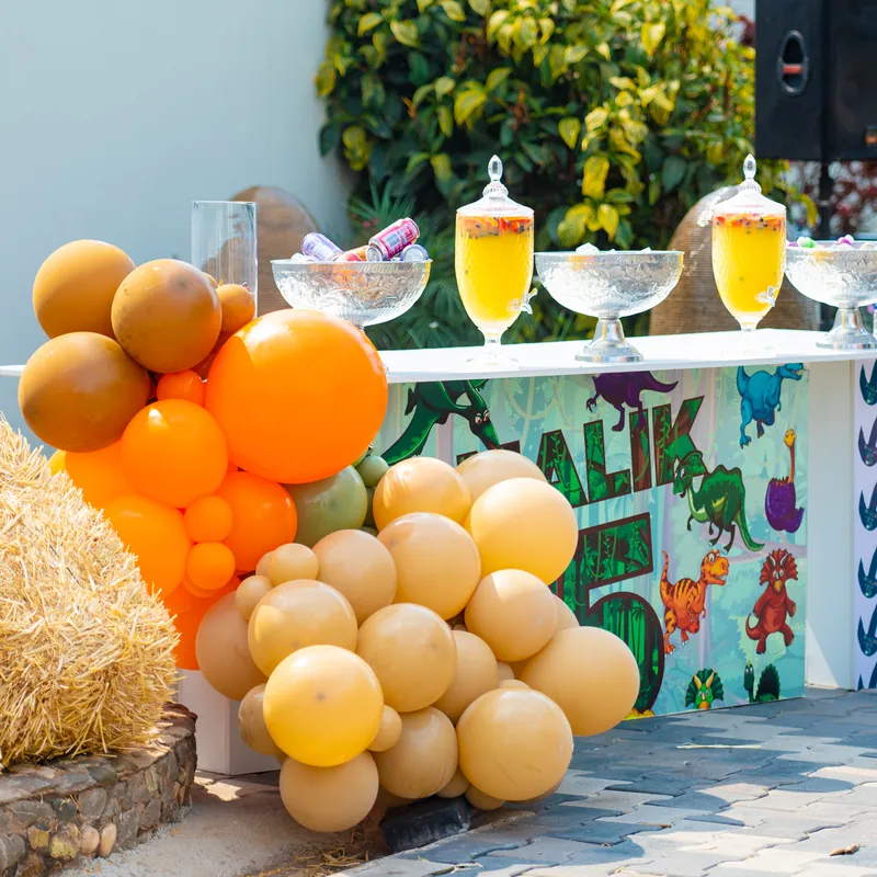 Dinosaur-themed drinks station with warm-toned balloons