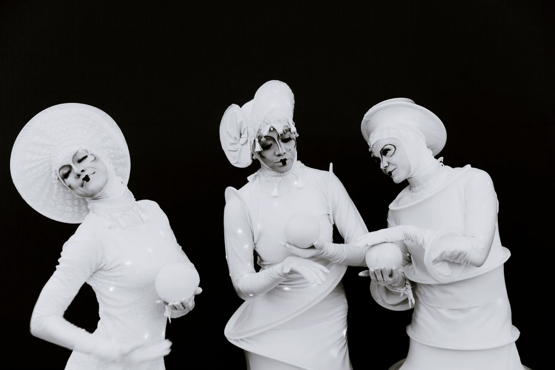Three white-costumed performers posing against a black background