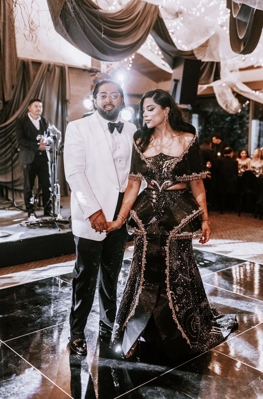 The couple walking hand in hand across the reception dance floor