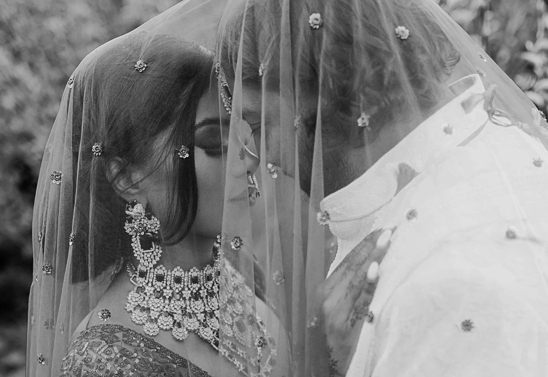 Black-and-white portrait of the couple beneath a beaded veil